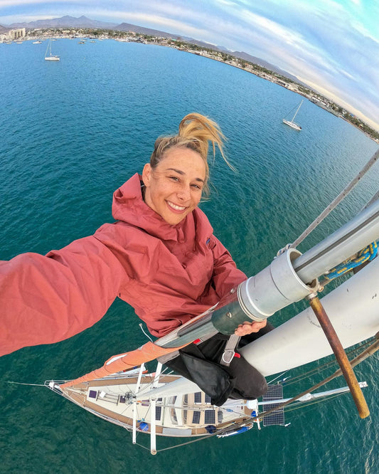 Hannah Goldberg taking a selfie while working at the top of a sailboat mast above the harbor