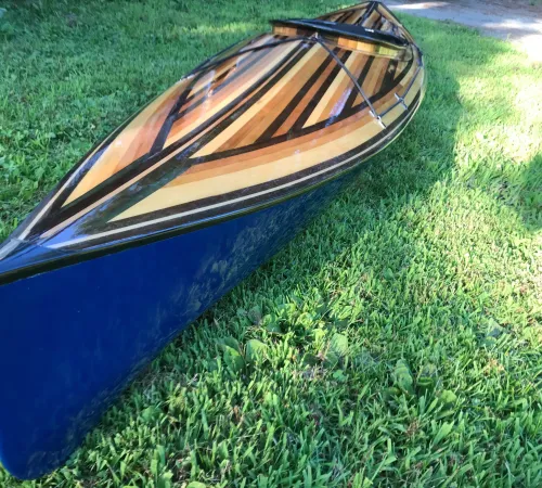 Handcrafted wooden kayak with a high-gloss finish displayed on grass during summer